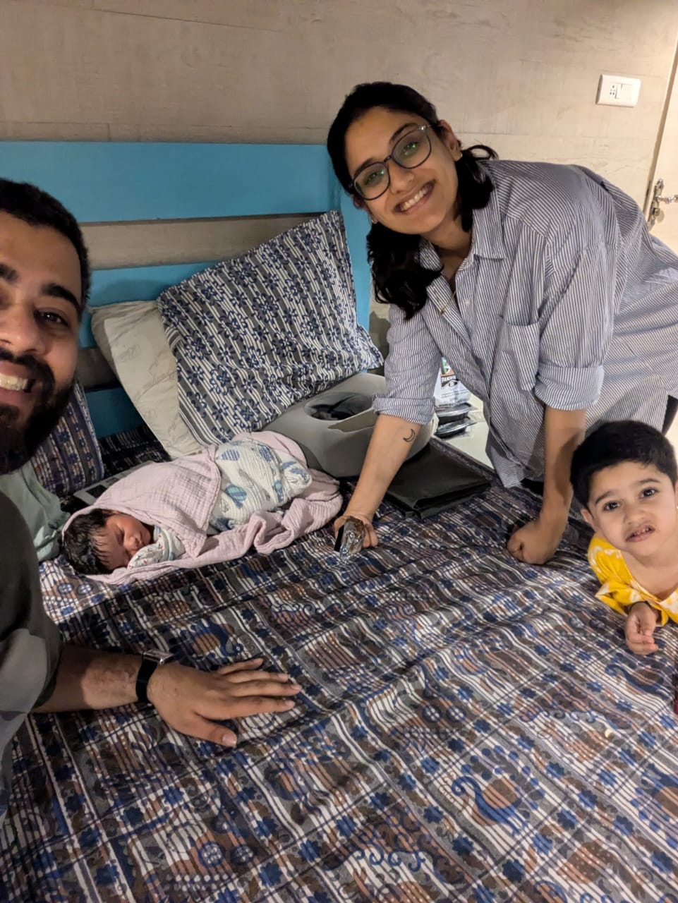 Meera and her husband smiling beside their newborn and older child
