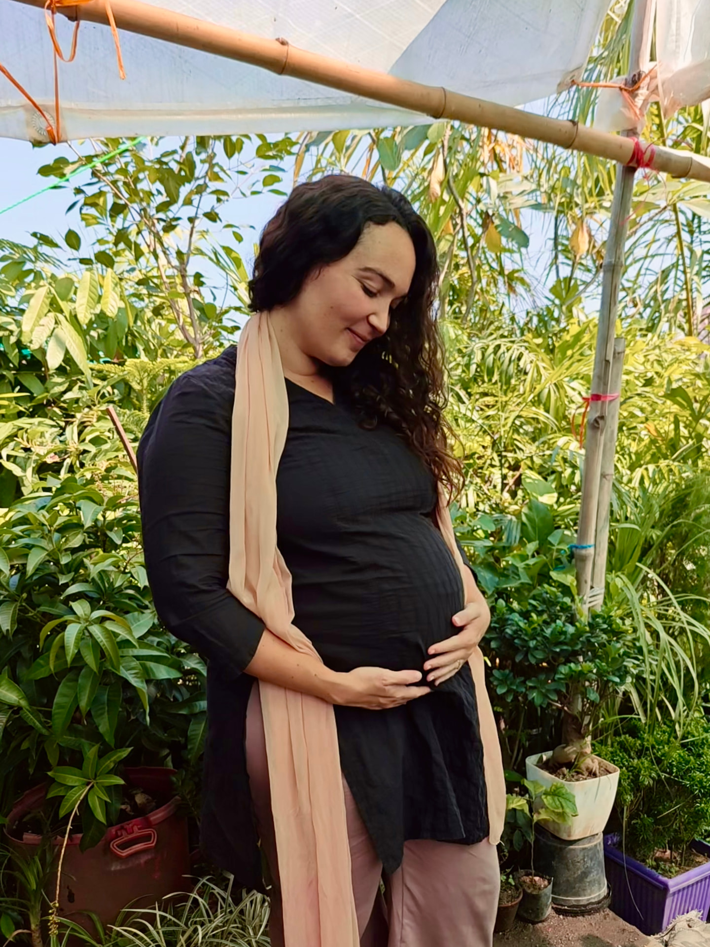 Megan holding her pregnant belly among plants at home