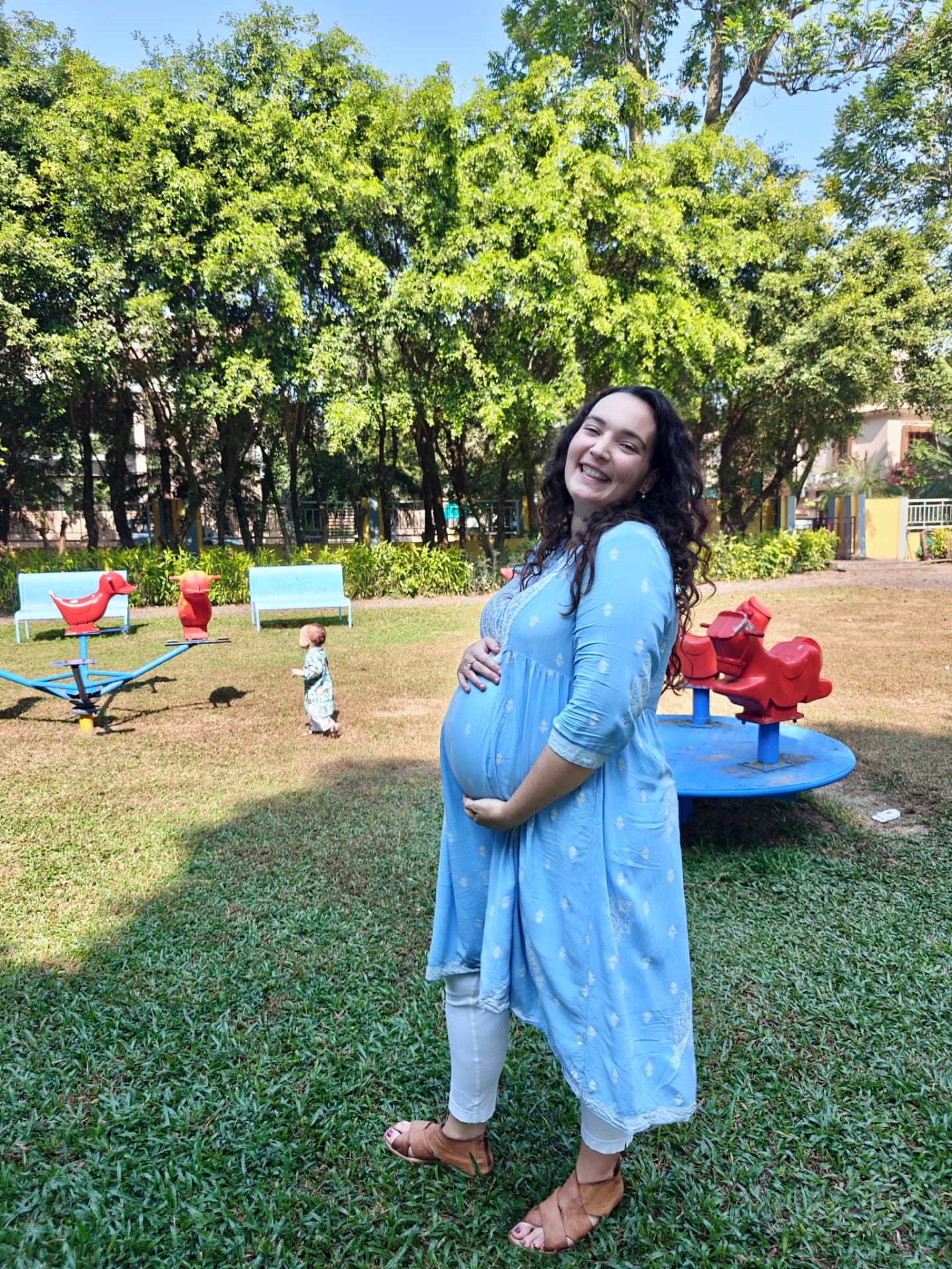 Megan smiling during pregnancy in a park with her older child nearby