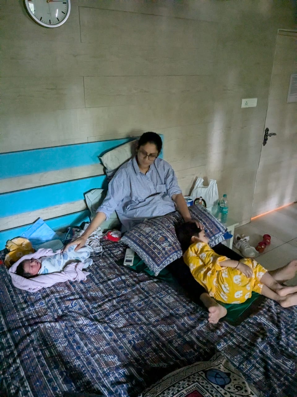 Meera resting at home with her newborn and her older child beside her